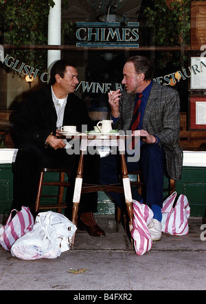 Don Henderson Actor Michael Elphick actor sitting at pavement cafe table with shopping bags talking and smoking a cigarette Stock Photo