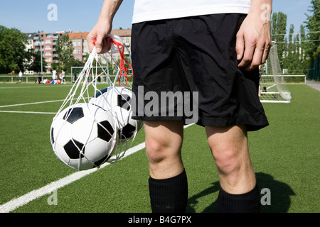 A young man carrying two soccer balls in a net, mid Stock Photo