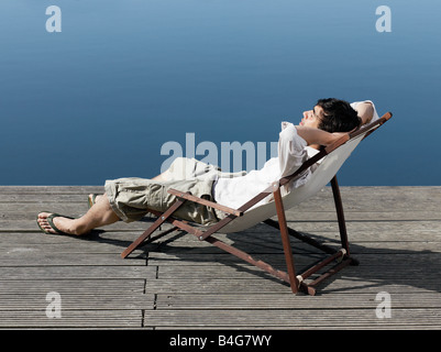 A young man sitting in a deck chair on a jetty Stock Photo