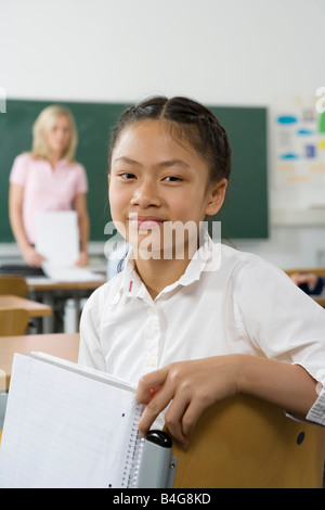 A pre-adolescent girl sitting in the back of a classroom, looking at camera Stock Photo