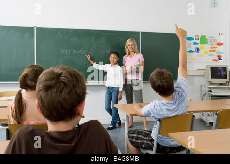 A teacher and a student at the blackboard, facing the class Stock Photo