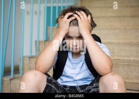 A worried pre-adolescent boy sitting on stairs in a school