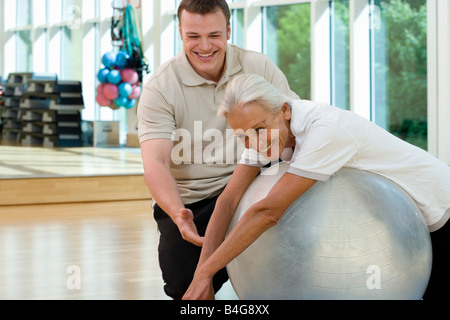 A senior woman on an exercise ball working with a trainer Stock Photo