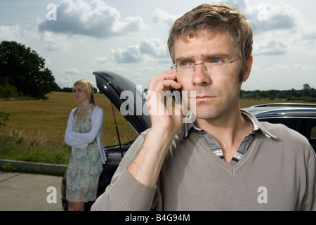 A couple standing at the roadside next to their broken down car Stock Photo