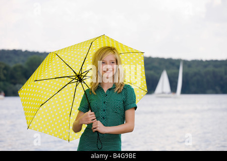 A young girl standing by a lake under an umbrella, overcast Stock Photo