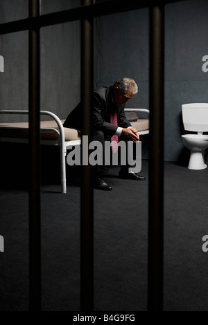 A businessman sitting on a bed in a prison cell Stock Photo