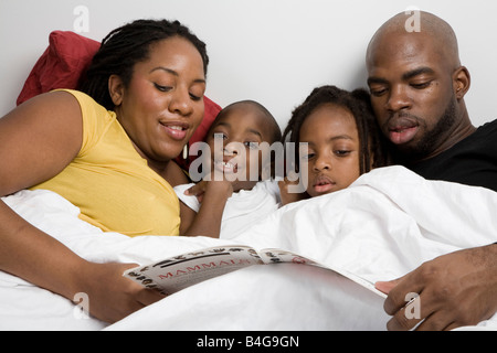 A family of four lying in bed reading a children's book Stock Photo
