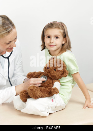 Female pediatrician examining a girl's teddy bear Stock Photo