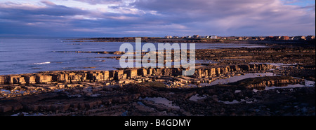 Beadnell, Northumberland, UK. View across the beach towards village with rock ledge in the foreground in evening light in August Stock Photo