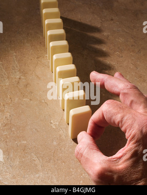 close up of hand poised to knock over dominoes Stock Photo
