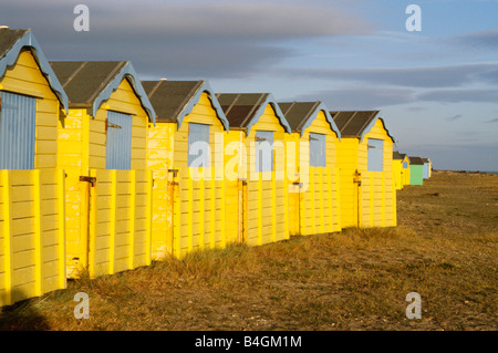 Row of bright yellow painted wooden beach huts on the beach at Folkestone in Kent Stock Photo