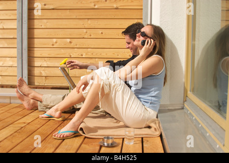 Side profile of young woman talking on mobile phone with young man using laptop beside her Stock Photo