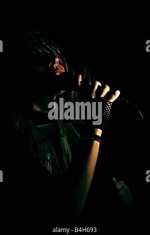 Blonde gothic singer wearing black, singing on stage with microphone. Stock Photo