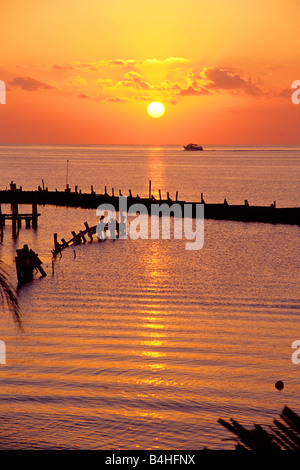 Tropical island sun rises over a pier as a ferry boat crosses the tranquil Caribbean sea in Cancun Mexico Central America Stock Photo