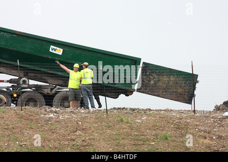 Waste Management Landfill workers with a backhoe placing dirt on trash ...