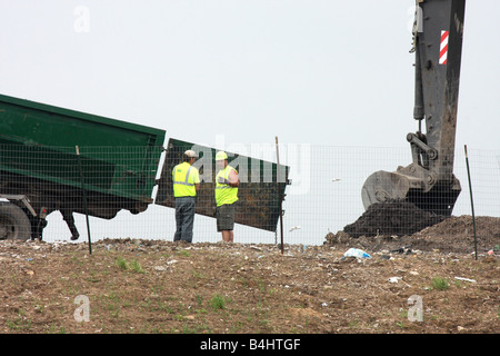 Waste Management Landfill workers with a backhoe placing dirt on trash ...