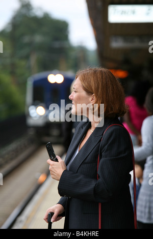 Commuting businesswoman keeps busy while awaiting the arrival of her train Stock Photo