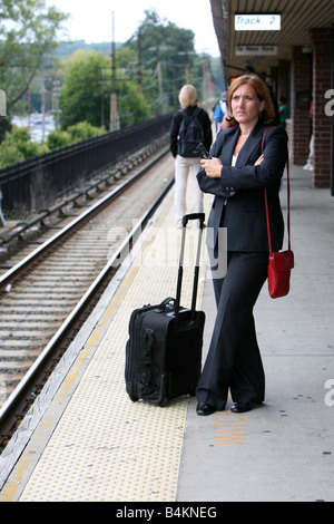 Commuting businesswoman keeps busy while awaiting the arrival of her train Stock Photo