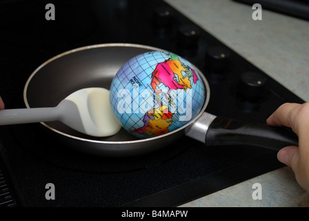 A globe is shown being fried in a skillet on a stove burner representing the concept of Global Warming Stock Photo
