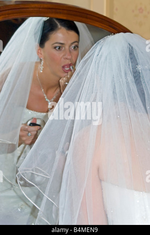 Vertical close up portrait of a young bride putting the finishing touches to her lipstick before her wedding Stock Photo