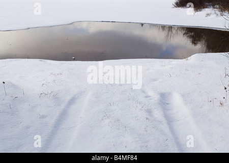 A pair of tire tracks in the snow stop short of open water on a lake in Michigan s Upper Peninsula Stock Photo