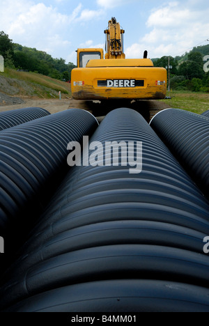 A John Deere construction excavator amidst long construction pipes Stock Photo