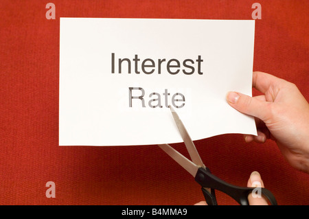 Picture of person cutting a piece of paper with 'Interest Rate' written on it using a pair of scissors Stock Photo