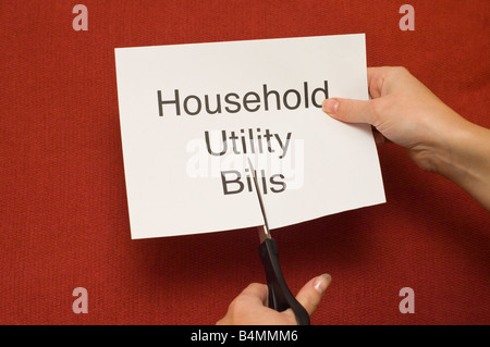 Picture of person cutting a piece of paper with 'Household utility bills' written on it using a pair of scissors Stock Photo