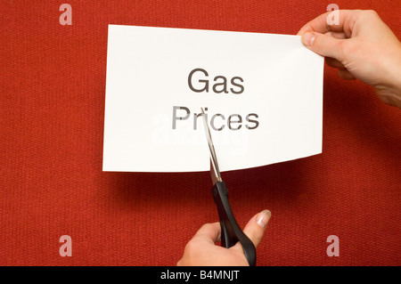 Picture of person cutting a piece of paper with 'Gas prices' written on it using a pair of scissors Stock Photo