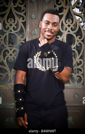 Stylish young black man wearing military style arm cuffs smiling at the camera standing in front of a decorative iron door. Stock Photo