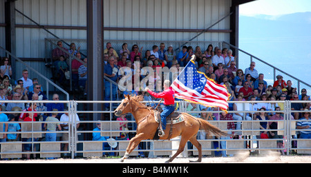 Cowboy carrying an American flag while riding on a horse at a rodeo Stock Photo