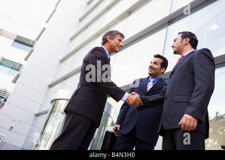 Three businessmen standing outdoors by building shaking hands and smiling (high key/selective focus) Stock Photo