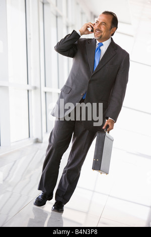 Businessman walking in corridor on cellular phone smiling (high key/selective focus) Stock Photo