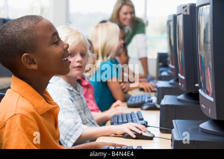 Six children at computer terminals with teacher in background (depth of field/high key) Stock Photo