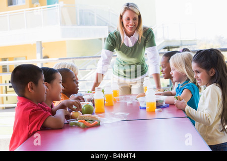 Teacher leaning on table outdoors while students eat lunch (high key) Stock Photo