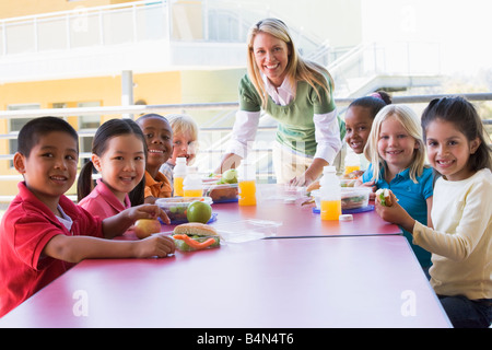 Teacher leaning on table outdoors while students eat lunch (high key) Stock Photo