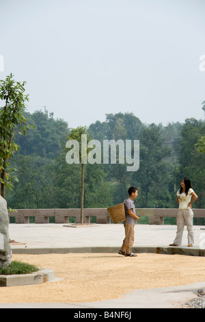 A Chinese boy carrying a basket in Dazu, China.  The grain on the road is rice drying in the sun Stock Photo