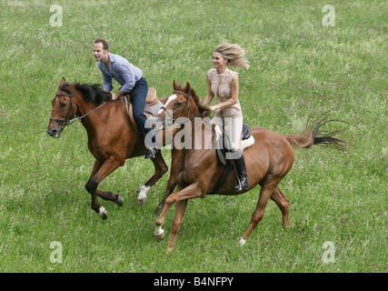 Couple galopping on horseback across a green meadow. Stock Photo