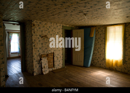 An empty bedroom with a blue mattress, door, windows, wooden floor and dirty wallpaper in an abandoned farm house. Stock Photo