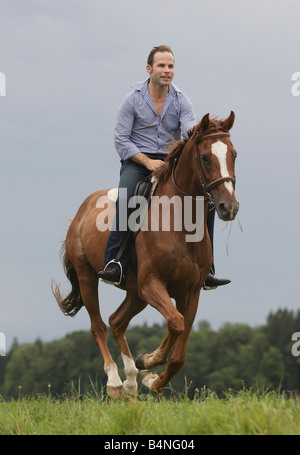 Man galopping on horseback across a green meadow. Stock Photo