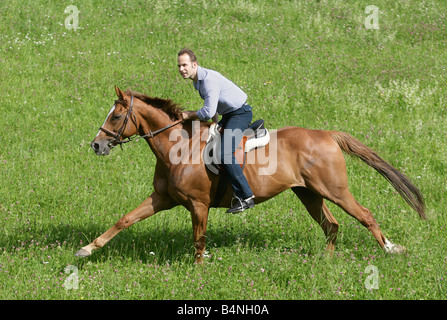 Man galopping on horseback across a green meadow. Stock Photo