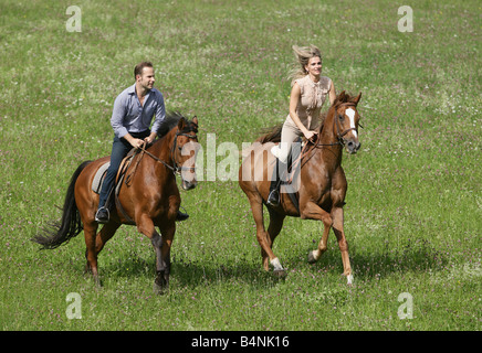 Couple galopping on horseback across a green meadow. Stock Photo