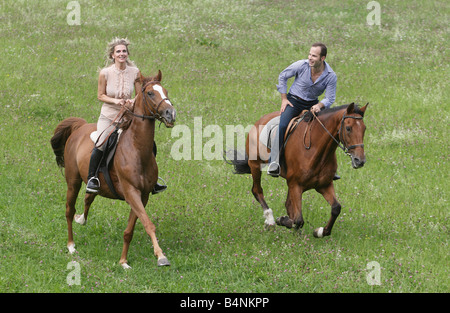 Couple galopping on horseback across a green meadow. Stock Photo