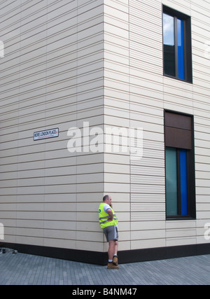 A construction worker standing on the corner of the building he is working on (Tower Bridge Hilton, London) makes a phone call Stock Photo