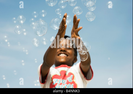 Indian boy playing with bubbles against blue sky. Andhra Pradesh, India Stock Photo