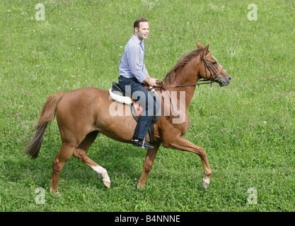 Man riding on horseback across a green meadow. Stock Photo