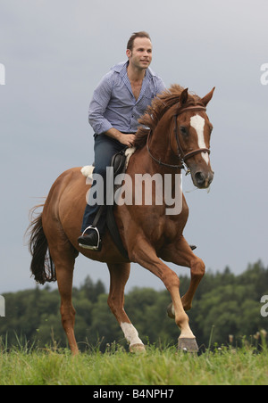 Man galopping on horseback across a green meadow. Stock Photo