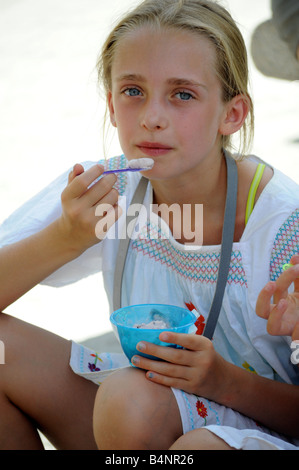 Royalty free photograph of young girl on holiday eating ice cream from a tub and licking spoon on a hot italian day out in Rome. Stock Photo