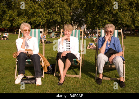 3 elderly women sitting on deckchairs in Hyde Park, London UK Stock Photo