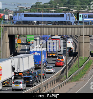 Transport choice M25 motorway nose to tail slow moving traffic watching fast passenger train on railway bridge junction 28 Brentwood Essex England UK Stock Photo